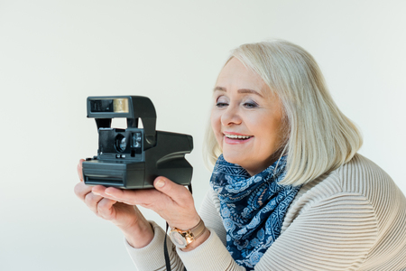 portrait of smiling senior woman holding retro photo camera