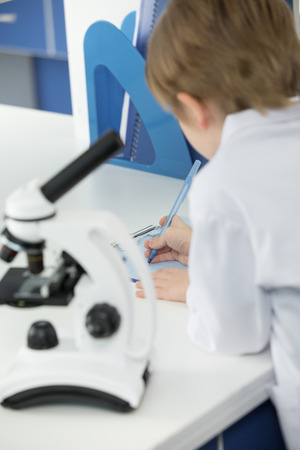 Schoolboy in white lab coat taking notes during scientific experiment in laboratoryの写真素材