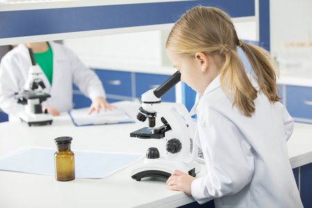 Schoolgirl in lab coat using microscopeの写真素材