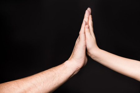Close-up partial view of father and child touching palms on black