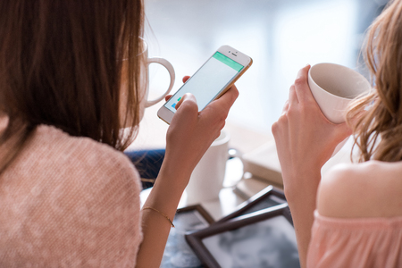 Rear view of two young women using smartphone and drinking teaの写真素材