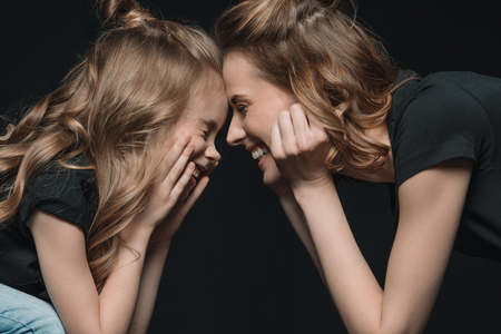 portrait of stylish daughter and mother smiling, touching foreheads and looking at each otherの写真素材