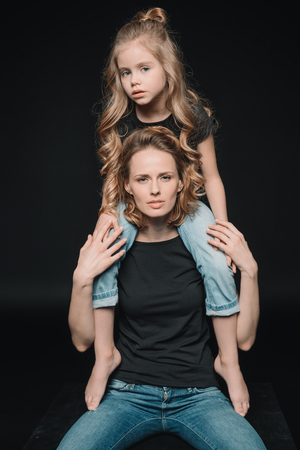 aughter sitting on mothers shoulders on blackの写真素材