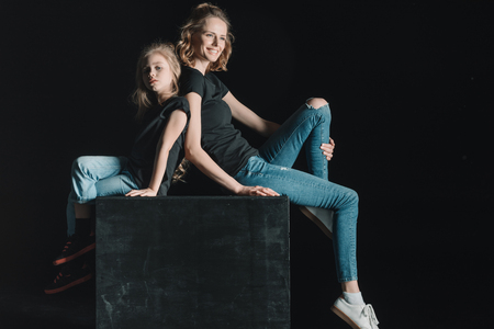 side view of stylish mother and daughter sitting on cubeの写真素材