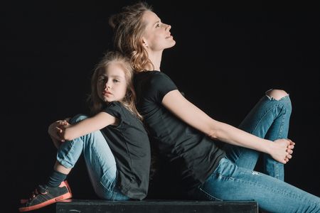 stylish mother and daughter sitting on cube on blackの写真素材