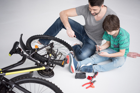 father and son with tools repairing bicycle together on whiteの写真素材