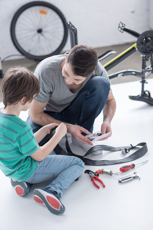 side view of father and son repairing bicycle tire togetherの写真素材