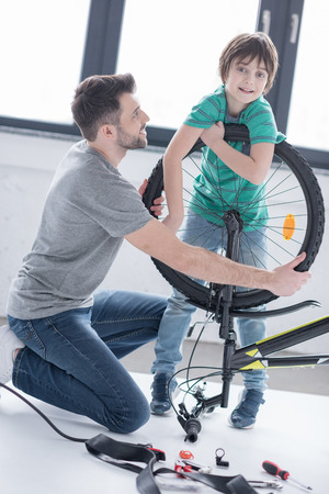 father and son repairing bicycle together on whiteの写真素材