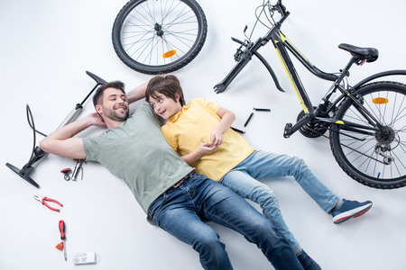 smiling father and son resting while fixing bicycle on whiteの写真素材