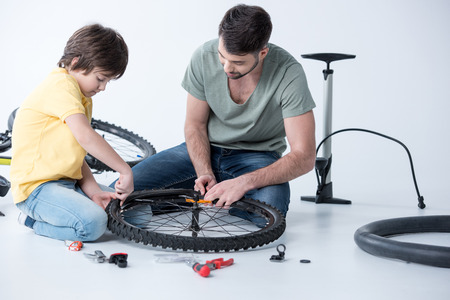 father and son with tools repairing bicycle wheelの写真素材