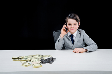 smiling boy playing businessman and talking on smartphone on blackの写真素材