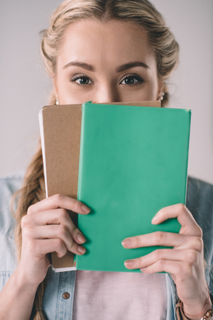 woman student covering face with notebooks in handsの写真素材