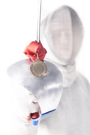Portrait of professional fencer in fencing mask holding medal and rapier