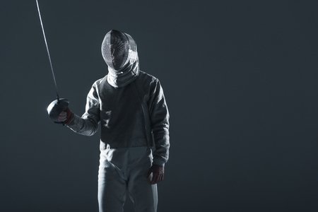fencer in fencing mask with rapier standing in position on grey