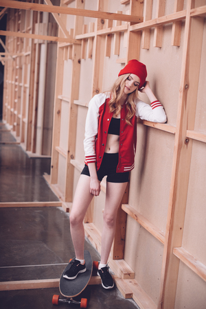hipster woman in baseball jacket with longboard posing at wooden wallの写真素材