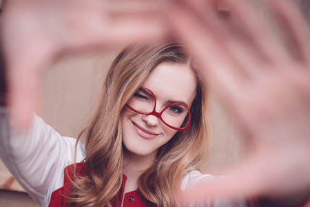 hipster woman with red eyeglasses making focus framing gesture and blinkingの写真素材
