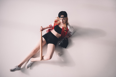 young sporty woman in cap lying with baseball equipmentの写真素材