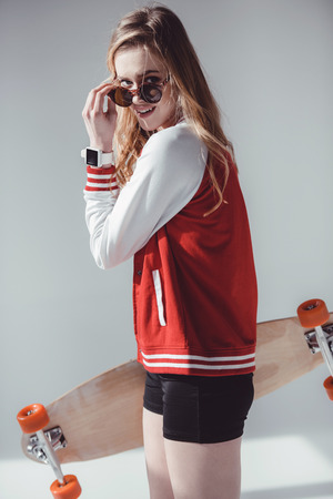 hipster woman with longboard and sunglasses posing in studio on greyの写真素材