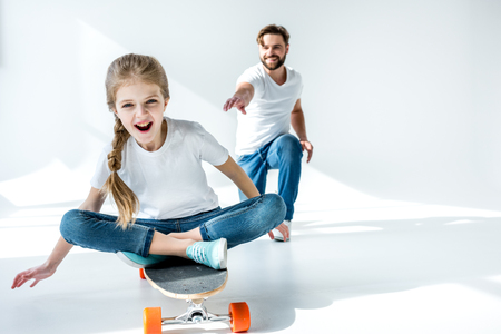 father looking at happy daughter sitting on skateboardの写真素材