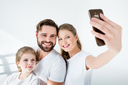 young family in white t-shirts taking selfie with smartphone in studioの写真素材