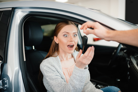 Person giving car key to excited woman sitting in car in dealership salonの写真素材