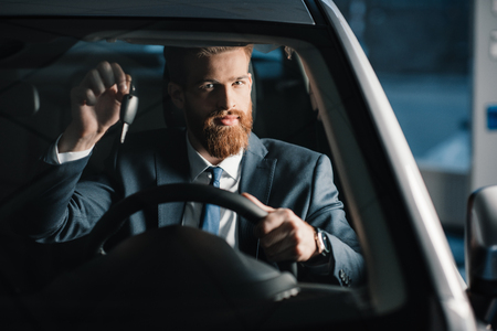 Bearded young businessman holding key while sitting in new carの写真素材