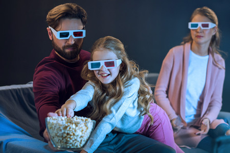 family in 3d glasses watching movie and eating popcornの写真素材