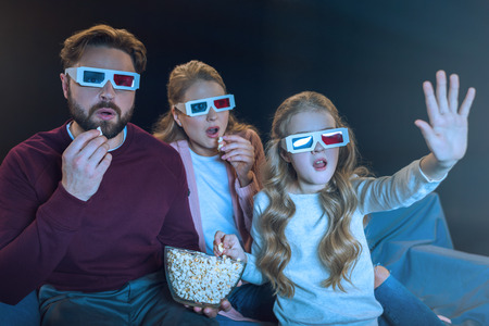 family in 3d glasses watching movie and eating popcornの写真素材