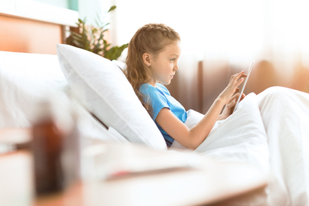 sick little girl using digital tablet in hospital bedの写真素材