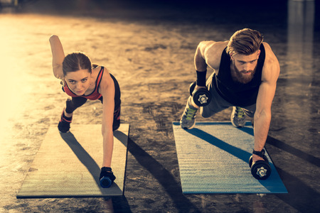 sporty man and woman doing plank exercise with dumbbells