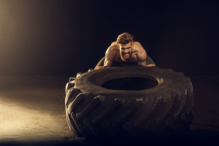muscular sportsman training with big tire on black with side lightingの写真素材