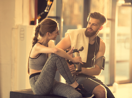 sportsman and sportswoman resting with towel and sport bottle