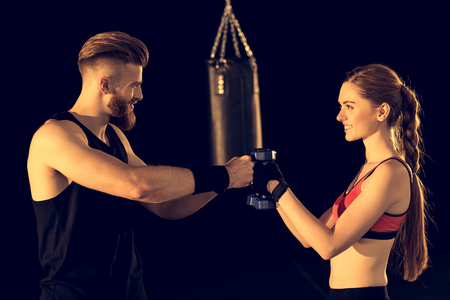 smiling sporty man and woman standing with dumbbells on blackの写真素材