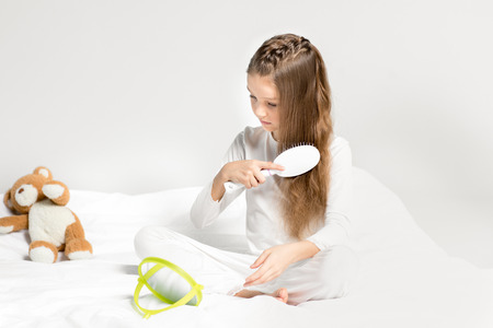 little girl in pajamas sitting on bed and combing hair