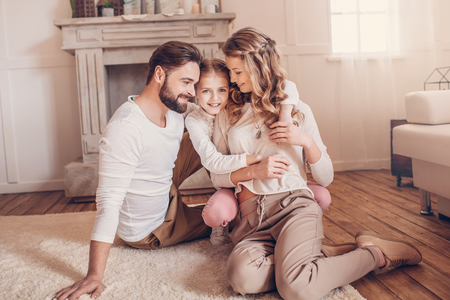 young family with one child sitting on carpet and hugging at homeの写真素材