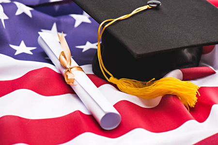 Close-up view of graduation mortarboard and diploma on US flagの写真素材