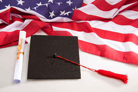 Close-up view of graduation mortarboard, diploma and us flag on whiteの写真素材