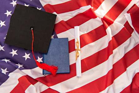 Top view of book, graduation mortarboard and diploma on US flag backgroundの写真素材