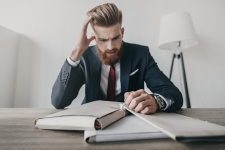 stressed businessman with documents and folders sitting at table in officeの写真素材
