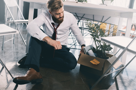 upset fired businessman sitting on floor in officeの写真素材