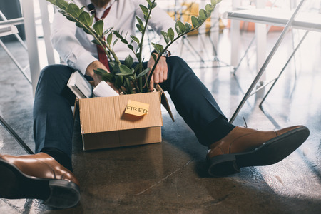 young fired businessman sitting on floor with belongings in boxの写真素材