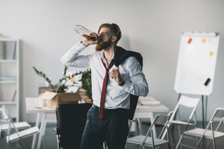 young businessman drinking whiskey from bottle in officeの写真素材