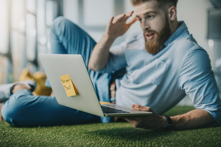bearded man lying on floor and using laptop in creative officeの写真素材