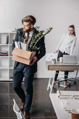 upset fired businessman with cardboard box in office, angry boss behindの写真素材