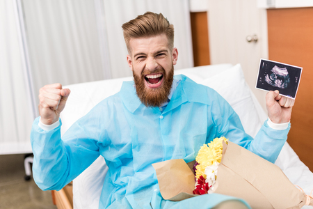 front view of happy young man with flowers and sonogram