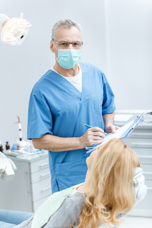 dentist holding folder in uniform with patient in dental clinicの写真素材