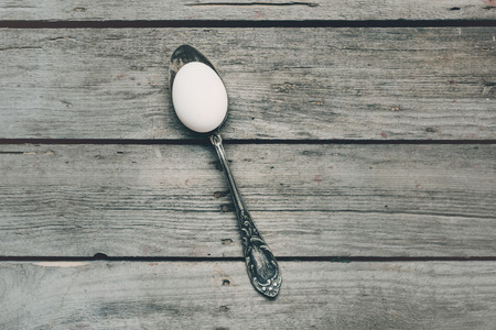 top view of white chicken egg in silver spoon on wooden tabletopの写真素材