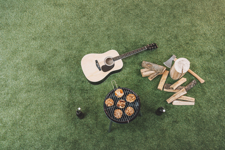 meat preparing on grill, beer bottles and guitar on grassの写真素材