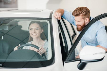 young woman sitting in new car and man standing nearの写真素材