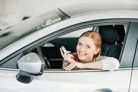 young woman with key sitting in new car